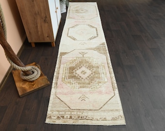 May include: A long, rectangular rug with a cream background and a brown and pink geometric pattern. The rug has a distressed look and is perfect for adding a touch of bohemian style to any room.