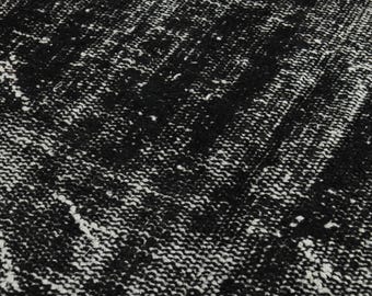 May include: Close-up of a black and white patterned rug. The rug has a textured surface with a distressed design. The pattern consists of dark black areas with white accents, creating a vintage or antique aesthetic.