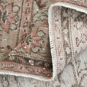 Puede incluir: Primer plano de una alfombra de color rosa y marr&oacute;n con flecos blancos. La alfombra est&aacute; doblada por la mitad, mostrando el reverso de la alfombra.