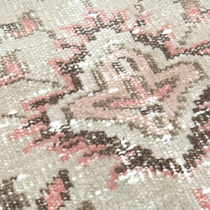 Puede incluir: Primer plano de una alfombra beige con un patr&oacute;n geom&eacute;trico rosa y marr&oacute;n. La alfombra tiene un aspecto desgastado y vintage.