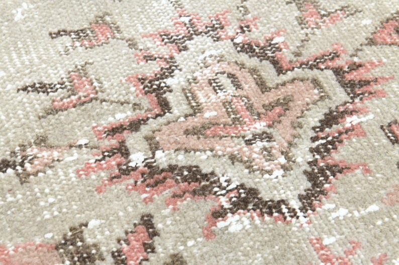 Puede incluir: Primer plano de una alfombra beige con un patr&oacute;n geom&eacute;trico rosa y marr&oacute;n. La alfombra tiene un aspecto desgastado y vintage.