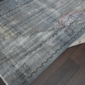 May include: A gray and white rug with a geometric pattern and colorful embroidery. The rug is folded in half and the edges are visible.