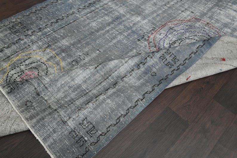 May include: A gray and white rug with a geometric pattern and colorful embroidery. The rug is folded in half and the edges are visible.