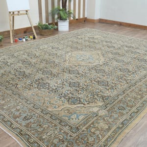 May include: Large, rectangular area rug with an intricate floral pattern in shades of beige, brown, and blue. The rug features a central medallion design and a detailed border. The rug is placed on a hardwood floor.