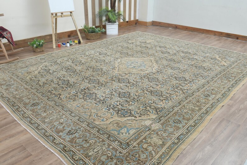 May include: Large, rectangular area rug with an intricate floral pattern in shades of beige, brown, and blue. The rug features a central medallion design and a detailed border. The rug is placed on a hardwood floor.