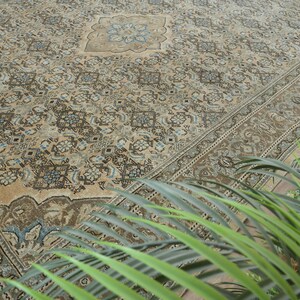 May include: An antique beige rug with an intricate floral pattern in shades of brown, blue, and cream. The rug features a central medallion design and a detailed border. The rug is a large size, suitable for a living room or dining area.
