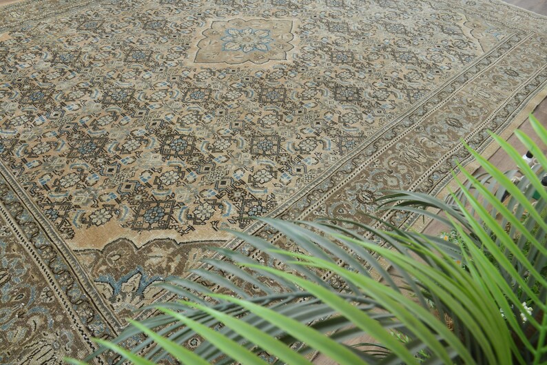 May include: An antique beige rug with an intricate floral pattern in shades of brown, blue, and cream. The rug features a central medallion design and a detailed border. The rug is a large size, suitable for a living room or dining area.