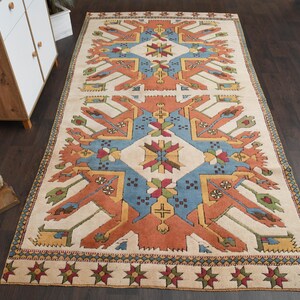 May include: A vintage rug with a geometric pattern in shades of red, blue, and white. The rug has a cream background and a border with a repeating star design.