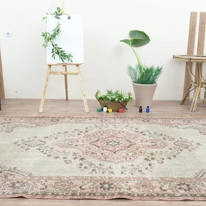 Puede incluir: Una alfombra vintage de color verde claro y rosa con un patr&oacute;n floral. La alfombra est&aacute; colocada sobre un suelo de madera en una habitaci&oacute;n con paredes blancas y detalles de madera.