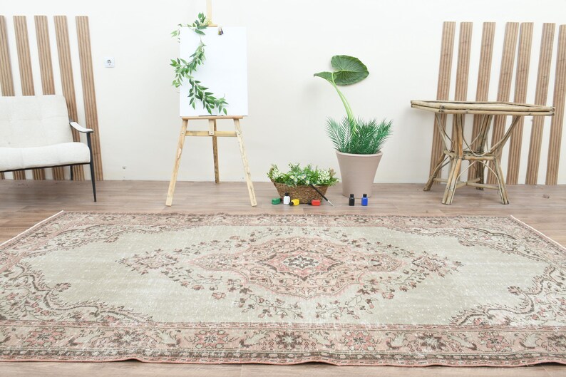 Puede incluir: Una alfombra vintage de color verde claro y rosa con un patr&oacute;n floral. La alfombra est&aacute; colocada sobre un suelo de madera en una habitaci&oacute;n con paredes blancas y detalles de madera.