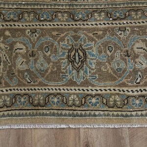 May include: Close-up of a section of a vintage rug with a detailed floral pattern. The rug features a brown and beige background with blue and black accents. The design includes stylized floral and geometric elements.