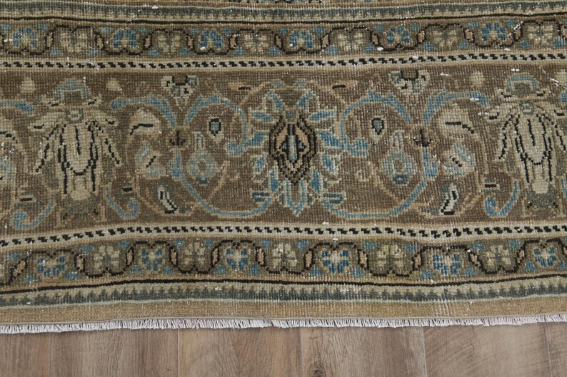May include: Close-up of a section of a vintage rug with a detailed floral pattern. The rug features a brown and beige background with blue and black accents. The design includes stylized floral and geometric elements.