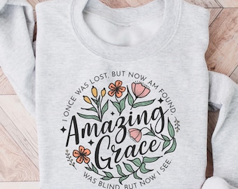 May include: A gray sweatshirt with a floral design and the text "I once was lost, but now am found. Amazing Grace. Was blind, but now I see."