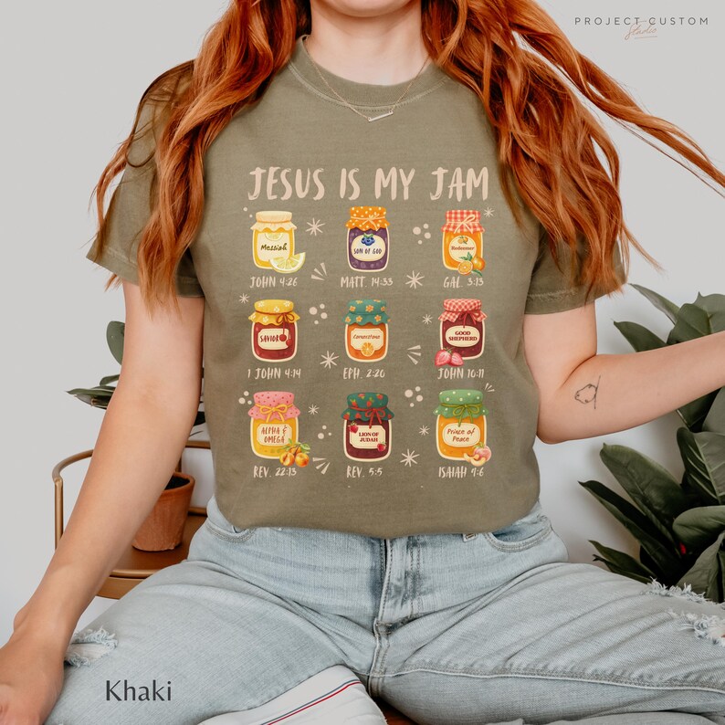 K&ouml;nnte beinhalten: Khaki-farbenes T-Shirt mit dem Text "JESUS IS MY JAM" und Illustrationen von Marmeladengl&auml;sern. Jedes Glas hat eine andere Geschmacksrichtung und einen Bibelvers. Lockere Passform.
