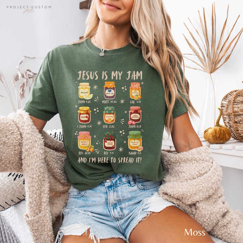 K&ouml;nnte beinhalten: Moosgr&uuml;nes T-Shirt mit dem Text "JESUS IS MY JAM" und Illustrationen von Marmeladengl&auml;sern. Das Shirt enth&auml;lt auch Bibelverse. Das Shirt ist aus einem weichen Material.