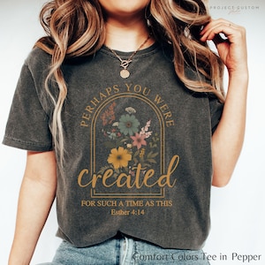 May include: A dark grey t-shirt with a floral design and the text "Perhaps you were created for such a time as this Esther 4:14".