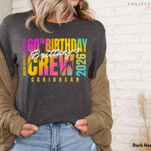 May include: Dark heather grey t-shirt with a colorful graphic. The graphic reads "60th Birthday Brittany's Crew Caribbean 2026" with palm trees. The shirt is a crew neck and has short sleeves.