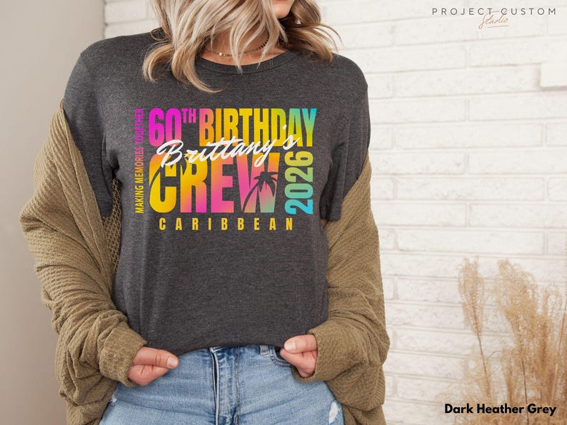 May include: Dark heather grey t-shirt with a colorful graphic. The graphic reads "60th Birthday Brittany's Crew Caribbean 2026" with palm trees. The shirt is a crew neck and has short sleeves.
