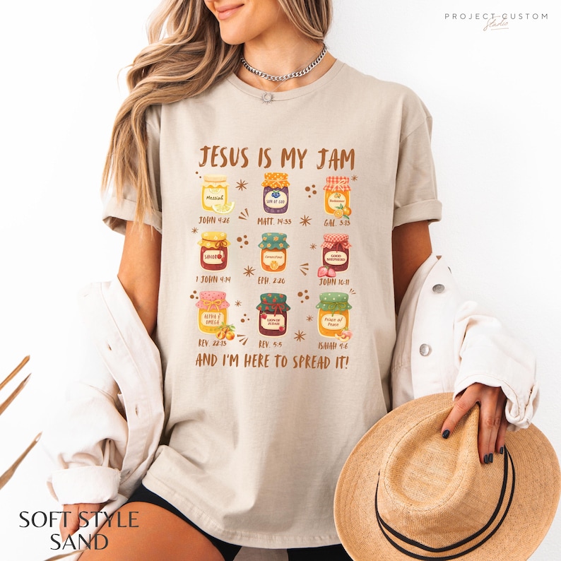 K&ouml;nnte beinhalten: Sandfarbenes T-Shirt mit dem Text "JESUS IS MY JAM" und Illustrationen von Marmeladengl&auml;sern. Das Shirt enth&auml;lt auch den Text "AND I'M HERE TO SPREAD IT!" und Bibelverse.