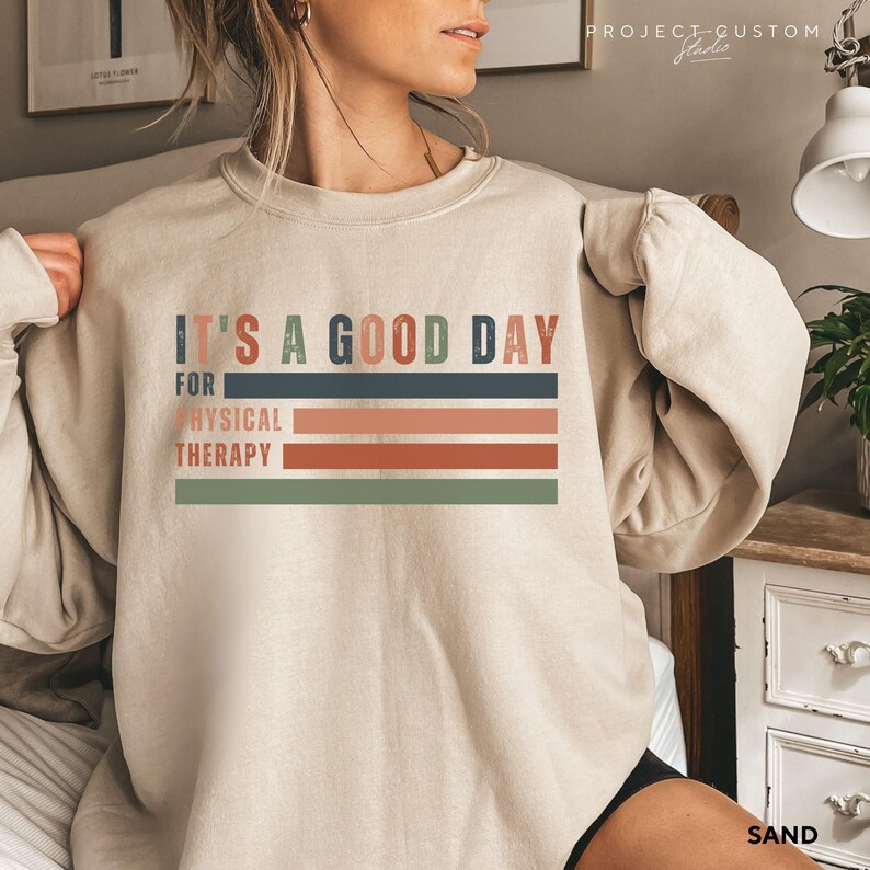 May include: A beige sweatshirt with the text "It's a good day for physical therapy" in a retro style with colorful stripes.