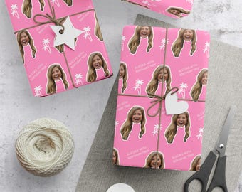 May include: Pink wrapping paper with a repeating pattern of a smiling woman's face, palm trees, and text that reads "ALICIA'S 40TH BIRTHDAY TRIP." The wrapped gifts are tied with twine and adorned with paper cutouts.