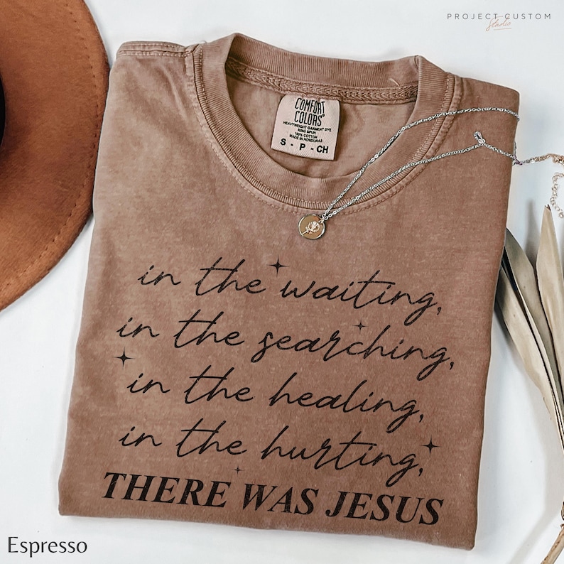 Pu&ograve; includere: Una maglietta marrone con il testo "in the waiting, in the searching, in the healing, in the hurting, THERE WAS JESUS" stampato in nero.