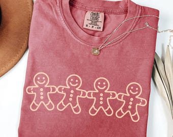 May include: A crimson colored t-shirt with a graphic of three gingerbread men holding hands. The shirt is made of a soft, comfortable fabric and has a vintage look.
