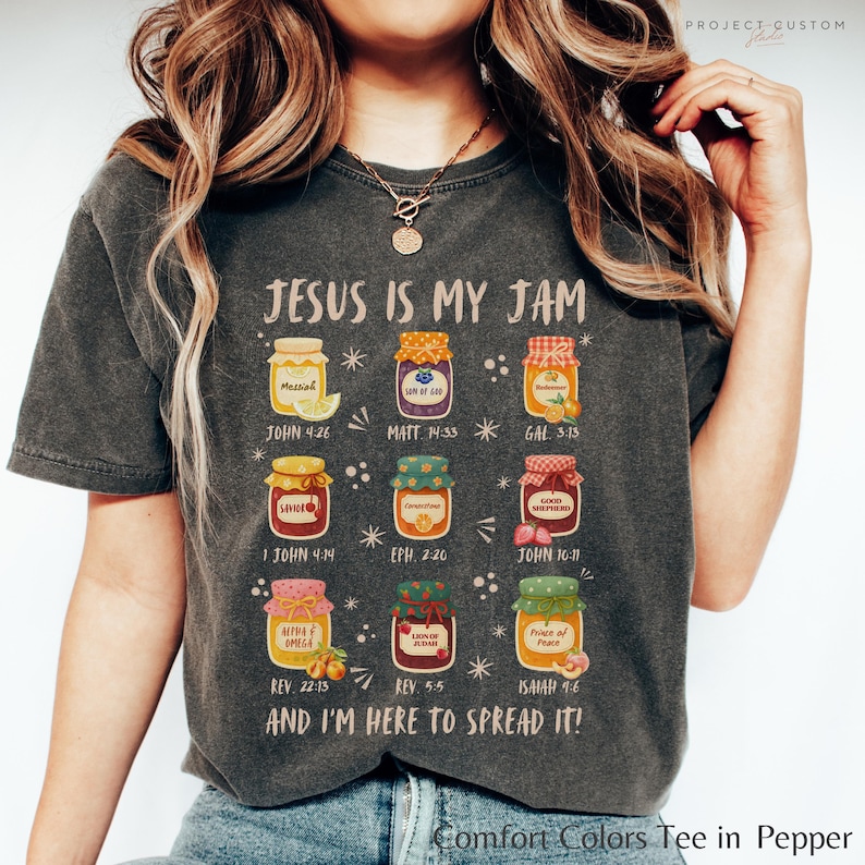 K&ouml;nnte beinhalten: Dunkelgraues Comfort Colors T-Shirt mit dem Text "JESUS IS MY JAM" und bunten Marmeladenglas-Illustrationen. Jedes Glas hat einen Bibelvers-Verweis. Das Shirt sagt auch "AND I'M HERE TO SPREAD IT!"