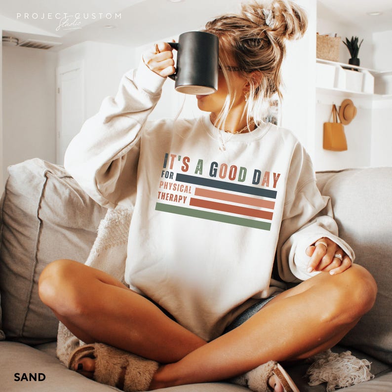 May include: A white sweatshirt with the text "It's a good day for physical therapy" in colorful retro-style lettering.