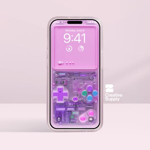 Puede incluir: Una funda transparente para teléfono con un diseño retro de videojuego rosa y morado. La pantalla del teléfono muestra la fecha y la hora. La funda presenta una cruceta, botones y detalles de placa de circuito. El logotipo de Creative Supply es visible.