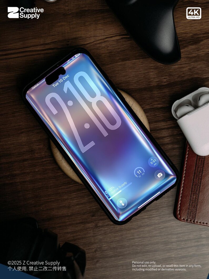 May include: A smartphone with a black case displays the time 2:18 on a gradient blue and purple screen. The phone rests on a wooden surface, with a wireless charger, a controller, and a pair of white earbuds nearby. The phone's screen displays the date, Tuesday, December 16.