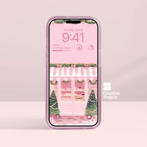 May include: A pink iPhone with a clear case displays a digital illustration of a pink bakery with Christmas decorations. The screen shows the time, date, and the text "Creative Supply".