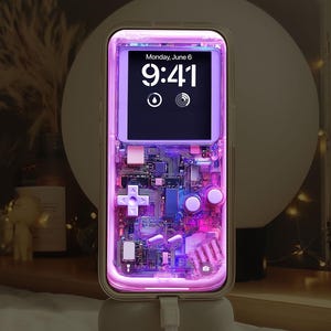 May include: A transparent phone case with a retro video game design, lit with purple and pink lights. The phone screen shows the time, "Monday, June 6, 9:41." The case features a cross-shaped directional pad and other game controller elements. The text "Creative Supply" is visible.