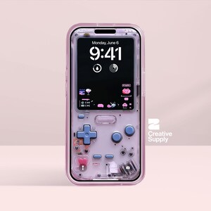 May include: A transparent phone case with a retro video game theme. The case has a pink frame and includes a cross-shaped D-pad, buttons, and a screen showing the time and date. The phone screen displays the time 9:41 and the date Monday, June 6.