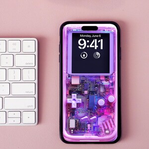 May include: A smartphone with a transparent case showing internal components. The screen displays "Monday, June 6" and the time "9:41". A white keyboard and rose gold headphones are in the background. The case has a retro game console design.