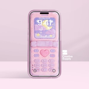 May include: A pink phone case with a fluffy texture, designed to resemble a flip phone. The screen displays a pastel-colored lock screen with a moon, stars, and the date. The case has a heart-shaped button and a clear border.