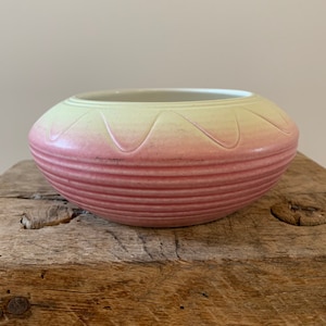 May include: A pink and green ceramic bowl with a textured, ribbed design. The bowl is round and has a wide, shallow shape.