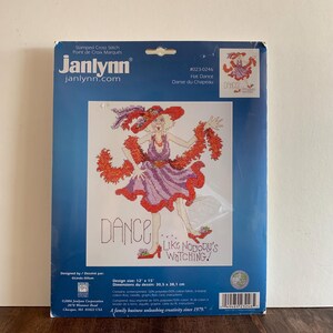 May include: A Janlynn stamped cross stitch kit titled "Hat Dance." The design features a woman in a purple dress and red boa, with the words "DANCE LIKE NOBODY'S WATCHING." The design size is 12 x 15 inches.