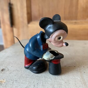 Puede incluir: Figurilla vintage de Mickey Mouse con un traje azul y zapatos rojos, sosteniendo un sombrero de copa negro. La figurita est&aacute; hecha de metal pintado y tiene una expresi&oacute;n caprichosa.
