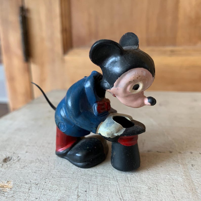 Puede incluir: Figurilla vintage de Mickey Mouse con un traje azul y zapatos rojos, sosteniendo un sombrero de copa negro. La figurita est&aacute; hecha de metal pintado y tiene una expresi&oacute;n caprichosa.
