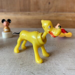 Puede incluir: Un perro de juguete de pl&aacute;stico amarillo con cola negra, labios rojos y ojos negros. El perro est&aacute; de pie sobre una superficie blanca.