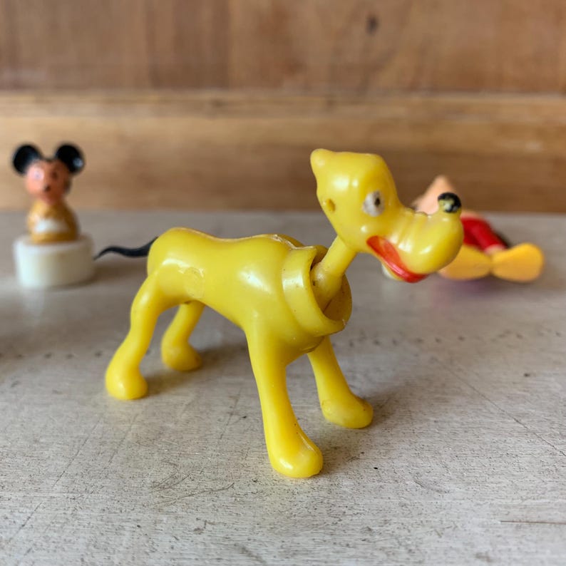Puede incluir: Un perro de juguete de pl&aacute;stico amarillo con cola negra, labios rojos y ojos negros. El perro est&aacute; de pie sobre una superficie blanca.