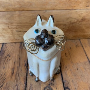 May include: White ceramic cat figurine with a black nose and blue eyes. The cat has gold wire whiskers.