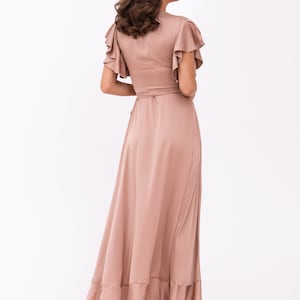 May include: A long, flowing maxi dress in a dusty rose colour. The dress has a V-neckline, short ruffle sleeves, and a wrap-style bodice. The skirt is gathered and has a ruffled hem.