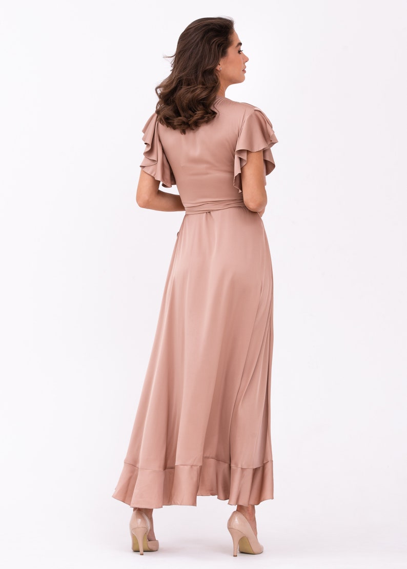 May include: A long, flowing maxi dress in a dusty rose colour. The dress has a V-neckline, short ruffle sleeves, and a wrap-style bodice. The skirt is gathered and has a ruffled hem.