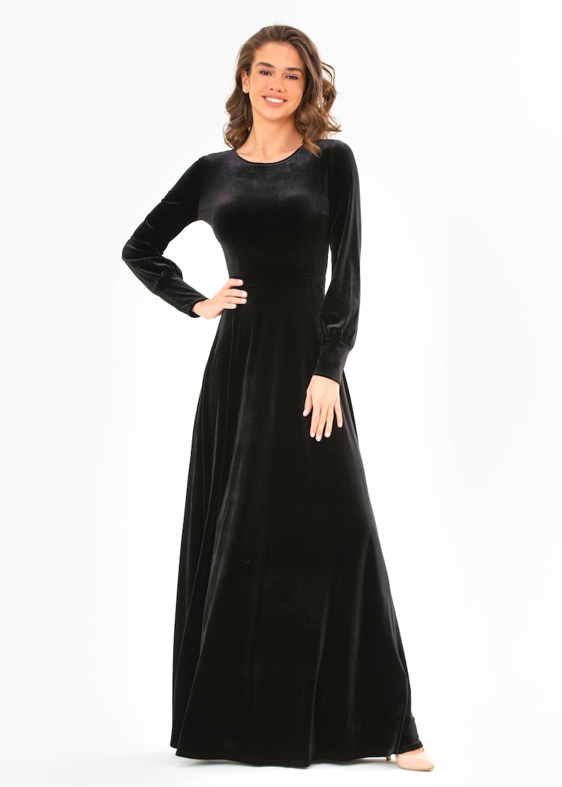 May include: A long-sleeved black velvet maxi dress with a round neckline. The dress has a fitted bodice and a flowing skirt.