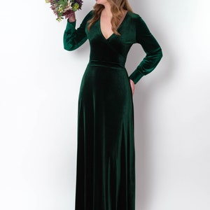 K&ouml;nnte beinhalten: Eine Frau in einem langen, smaragdgr&uuml;nen Samtkleid mit V-Ausschnitt und langen &Auml;rmeln. Sie h&auml;lt einen Blumenstrau&szlig;.