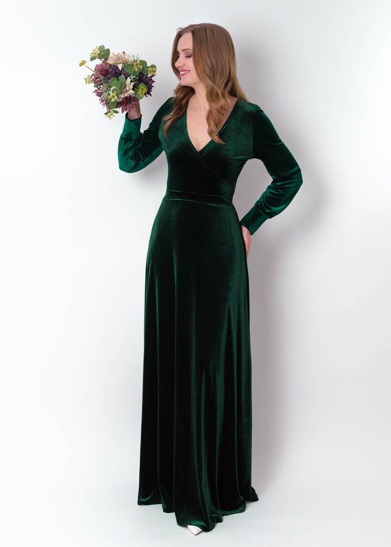K&ouml;nnte beinhalten: Eine Frau in einem langen, smaragdgr&uuml;nen Samtkleid mit V-Ausschnitt und langen &Auml;rmeln. Sie h&auml;lt einen Blumenstrau&szlig;.