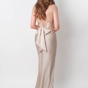 May include: A long, champagne-colored satin dress with a bow at the back.