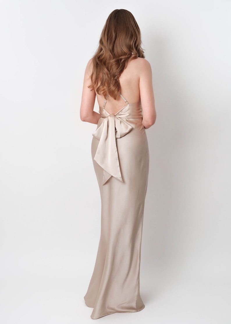 May include: A long, champagne-colored satin dress with a bow at the back.